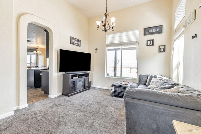 living area featuring carpet floors, plenty of natural light, arched walkways, and a notable chandelier