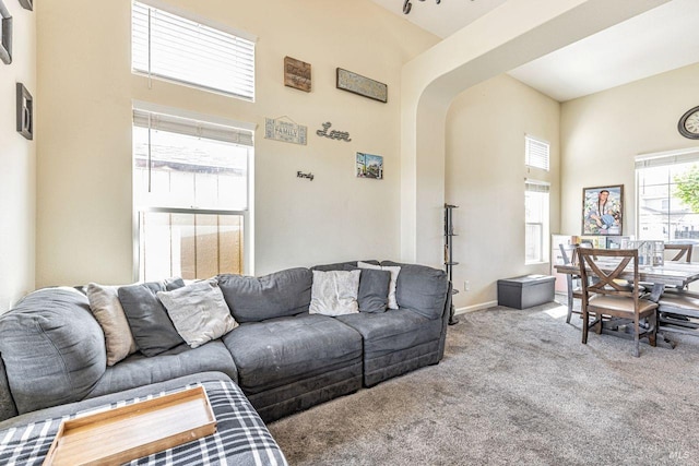 carpeted living room featuring baseboards, arched walkways, and a high ceiling