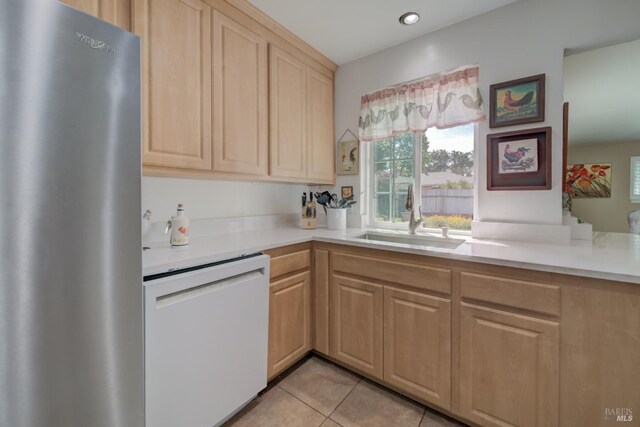kitchen featuring freestanding refrigerator, a sink, light brown cabinetry, and white dishwasher
