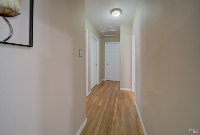 hallway featuring baseboards, attic access, and light wood-style flooring