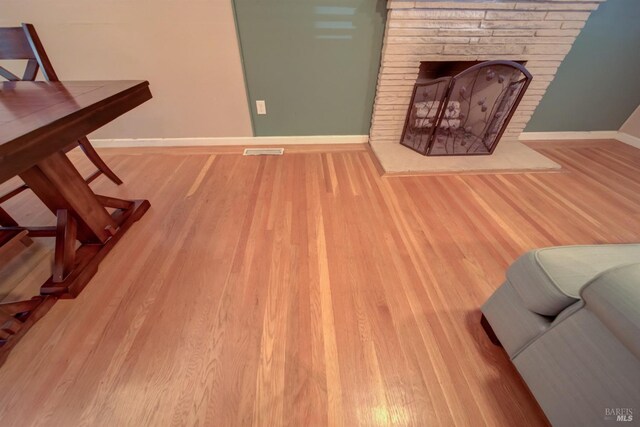 living room featuring baseboards, wood finished floors, visible vents, and a fireplace