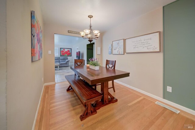 dining space with a chandelier, baseboards, visible vents, and light wood-type flooring