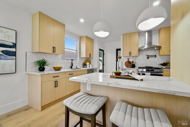 kitchen featuring light wood-style floors, light brown cabinets, wall chimney exhaust hood, and stainless steel gas stove