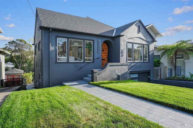 view of front facade featuring a shingled roof, fence, stucco siding, and a front yard