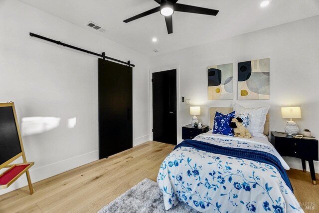 bedroom with a ceiling fan, visible vents, wood finished floors, a barn door, and baseboards