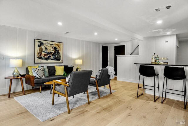 living area featuring a decorative wall, visible vents, and light wood-type flooring