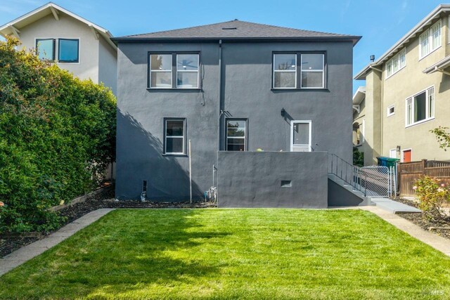 back of house featuring a lawn, stucco siding, and fence
