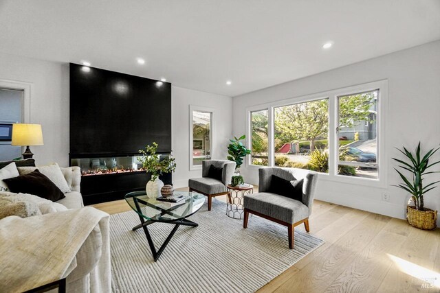 living room with recessed lighting, light wood finished floors, and a glass covered fireplace