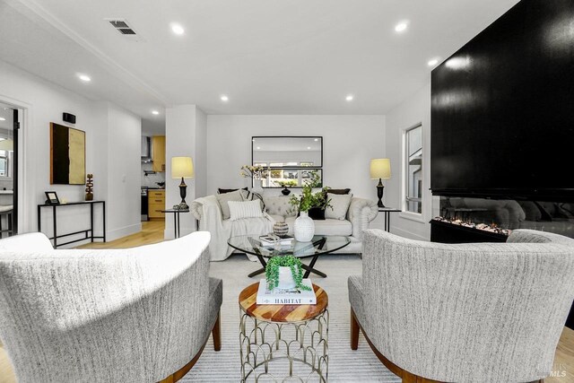 living area featuring a large fireplace, recessed lighting, light wood-style flooring, and visible vents