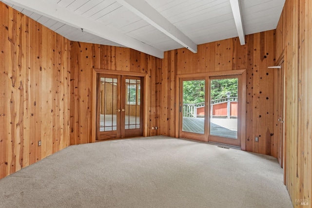 carpeted spare room with beamed ceiling, wood walls, french doors, and visible vents