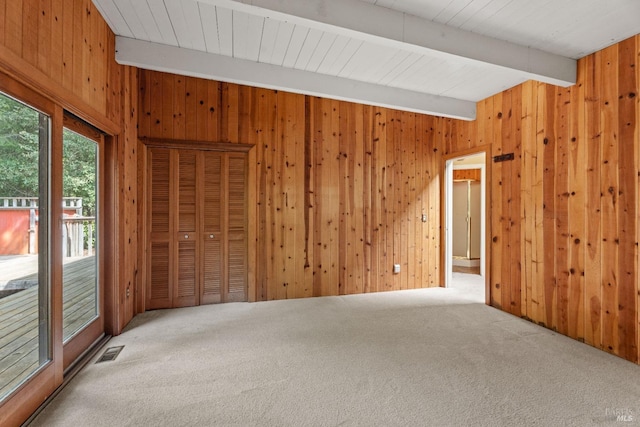 carpeted empty room featuring beamed ceiling, wood walls, and visible vents