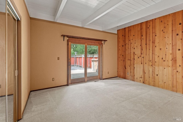 carpeted empty room featuring wooden walls and beamed ceiling