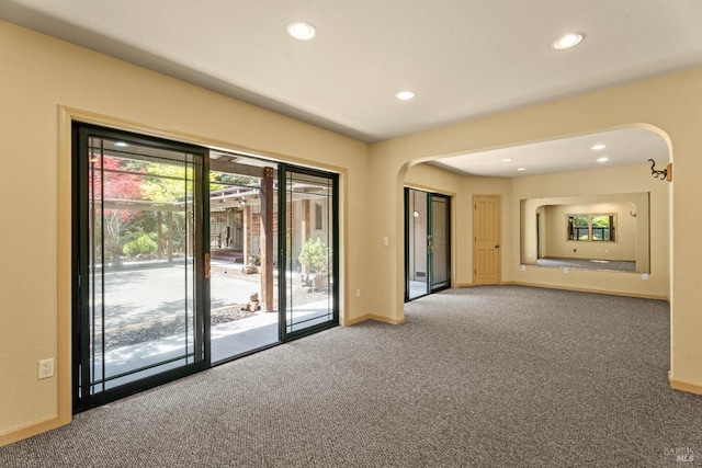 carpeted empty room featuring arched walkways, baseboards, and recessed lighting