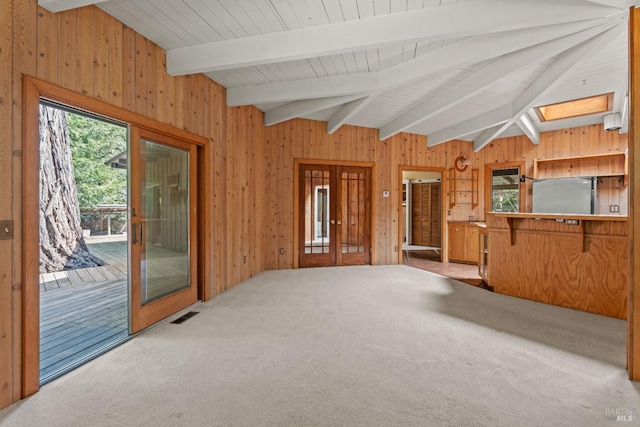 unfurnished living room with carpet floors, beamed ceiling, wood walls, and visible vents