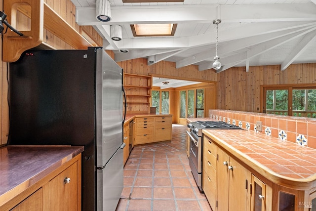 kitchen featuring appliances with stainless steel finishes, tile counters, wood walls, light tile patterned floors, and beamed ceiling