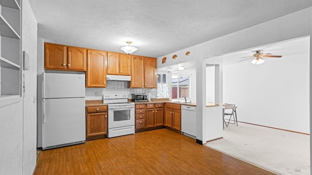 kitchen featuring wood finished floors, white appliances, ceiling fan, under cabinet range hood, and a sink