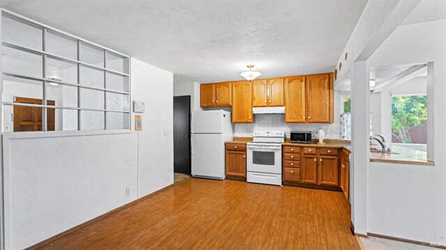 kitchen with white appliances, light countertops, under cabinet range hood, brown cabinets, and light wood-style flooring