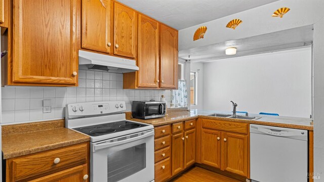 kitchen with white appliances, backsplash, under cabinet range hood, and a sink