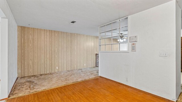 empty room featuring wood walls, visible vents, and wood finished floors