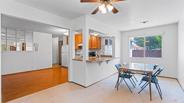 kitchen with brown cabinets, ceiling fan, a sink, freestanding refrigerator, and visible vents
