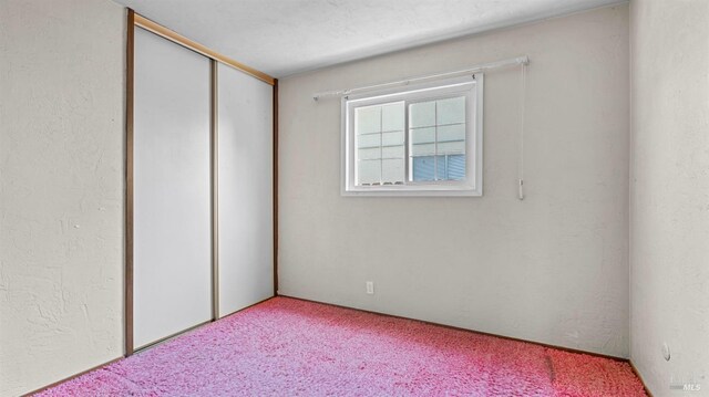 unfurnished bedroom featuring light colored carpet, a textured wall, and a closet