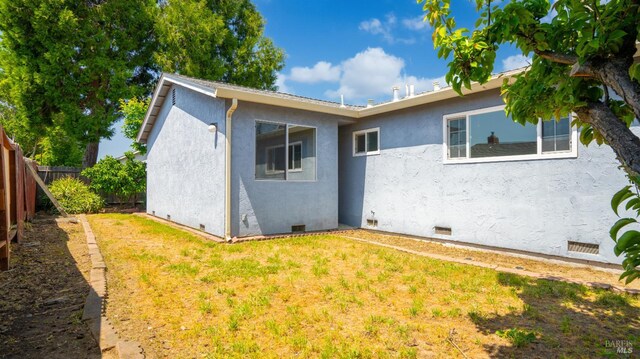 back of property with fence, stucco siding, a yard, and crawl space