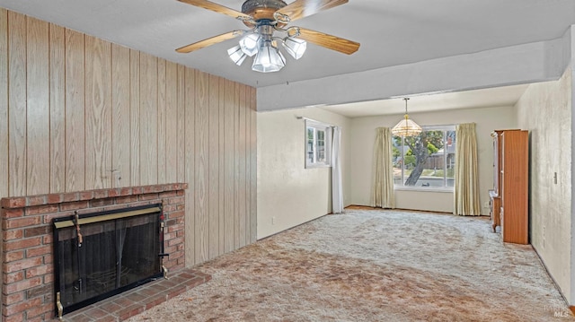 unfurnished living room featuring carpet floors, a ceiling fan, a brick fireplace, and wooden walls