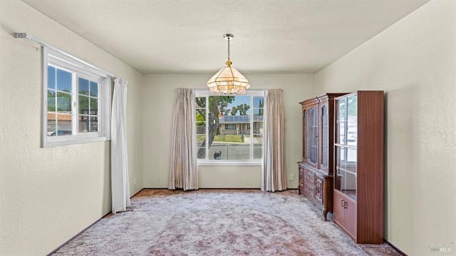 unfurnished dining area with a healthy amount of sunlight, carpet flooring, and a chandelier