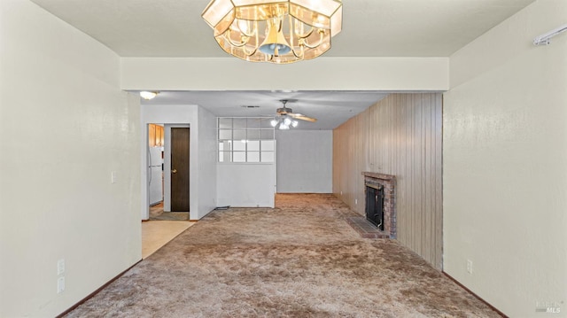 unfurnished living room with ceiling fan with notable chandelier, carpet flooring, and a brick fireplace