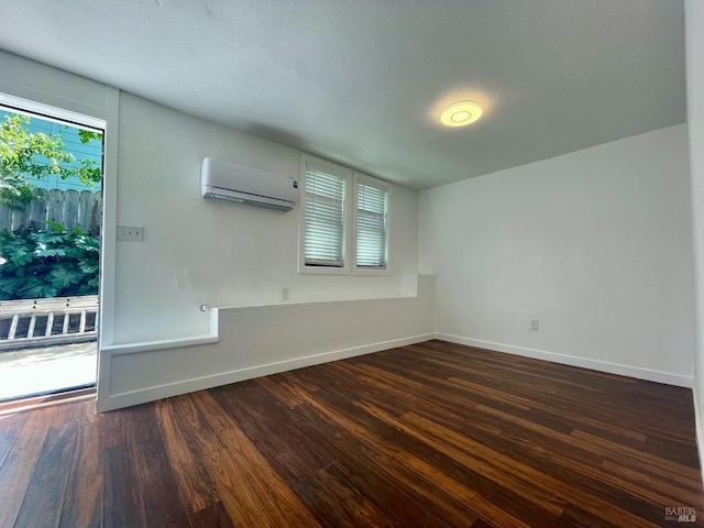 spare room with baseboards, an AC wall unit, and dark wood finished floors