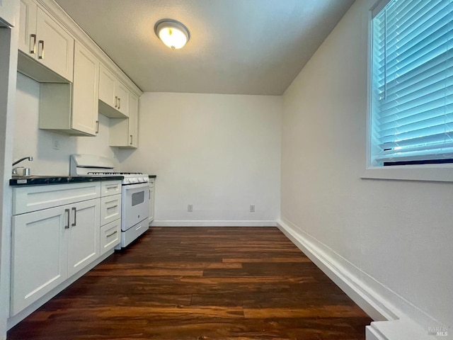kitchen with dark countertops, baseboards, white range with gas stovetop, white cabinets, and dark wood finished floors