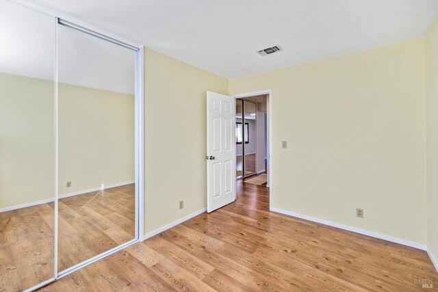unfurnished bedroom featuring baseboards, a closet, wood finished floors, and visible vents