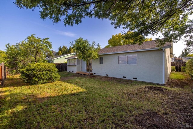 back of property with a lawn, fence, stucco siding, and crawl space