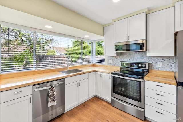 kitchen featuring decorative backsplash, wooden counters, a sink, light wood-style flooring, and stainless steel appliances