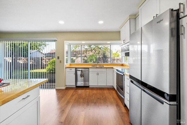 kitchen featuring butcher block counters, white cabinetry, a sink, light wood finished floors, and stainless steel appliances