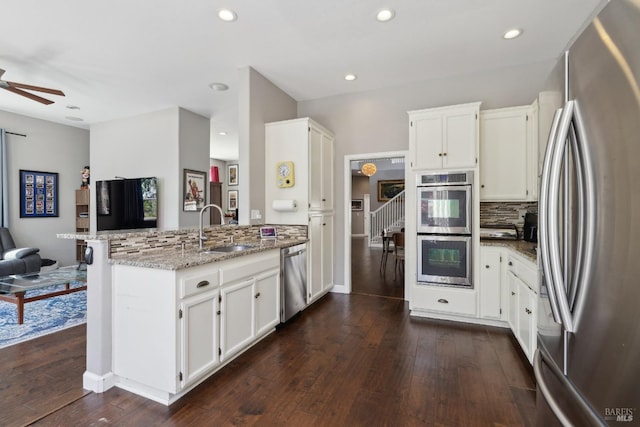kitchen featuring a peninsula, tasteful backsplash, light stone counters, a sink, and appliances with stainless steel finishes