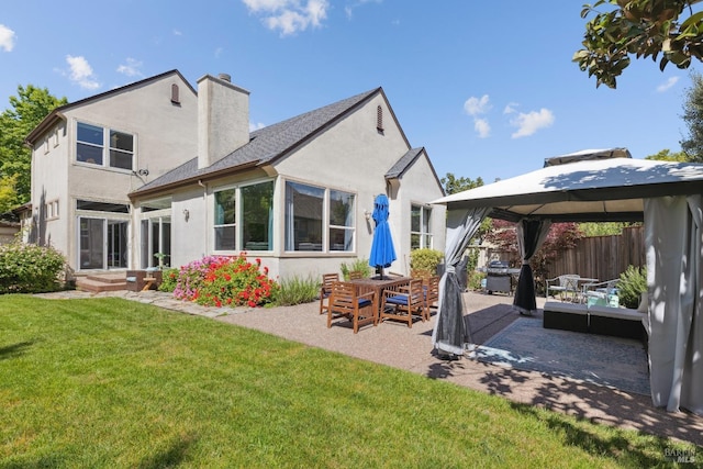 back of property featuring a gazebo, stucco siding, a chimney, a patio area, and a yard