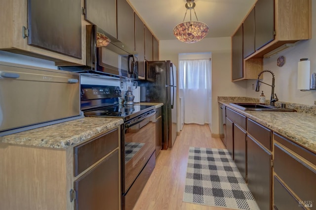 kitchen featuring pendant lighting, a sink, light countertops, black appliances, and light wood finished floors