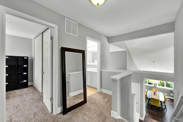 corridor with visible vents, an upstairs landing, baseboards, and carpet floors