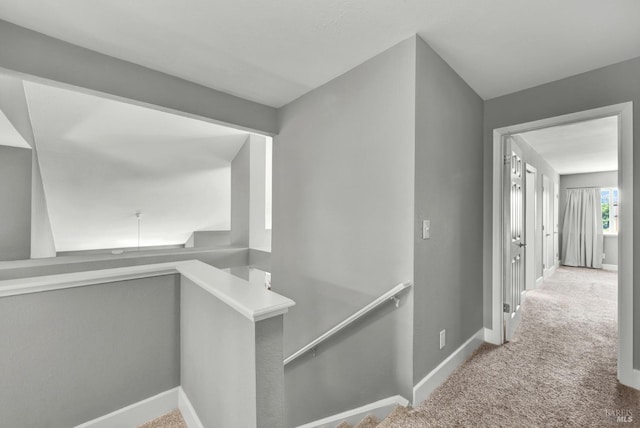 hallway featuring an upstairs landing, baseboards, and carpet floors