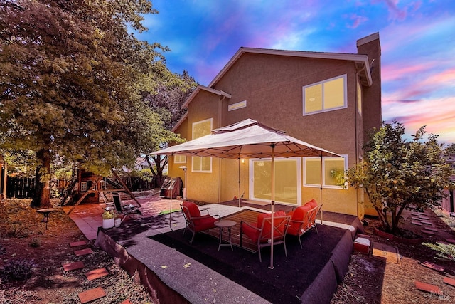 back of house at dusk with a patio, a chimney, and stucco siding