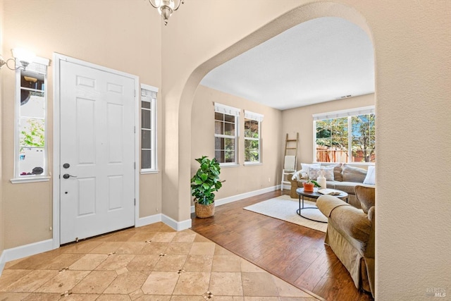 foyer entrance featuring arched walkways, baseboards, and light tile patterned flooring