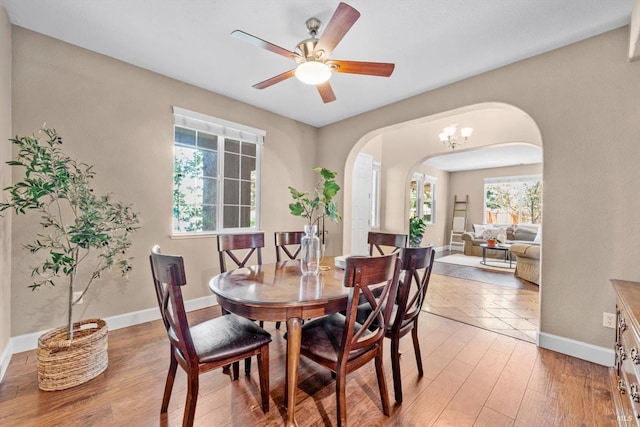 dining area featuring baseboards, arched walkways, a ceiling fan, and light wood-style flooring