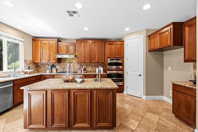 kitchen with light stone countertops, a sink, stainless steel appliances, backsplash, and a center island with sink