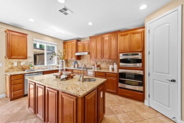 kitchen featuring appliances with stainless steel finishes, a sink, backsplash, visible vents, and a center island with sink