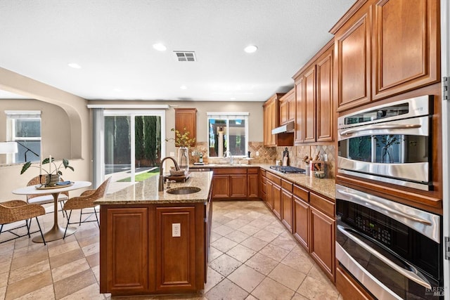 kitchen with a sink, stainless steel appliances, decorative backsplash, visible vents, and a center island with sink
