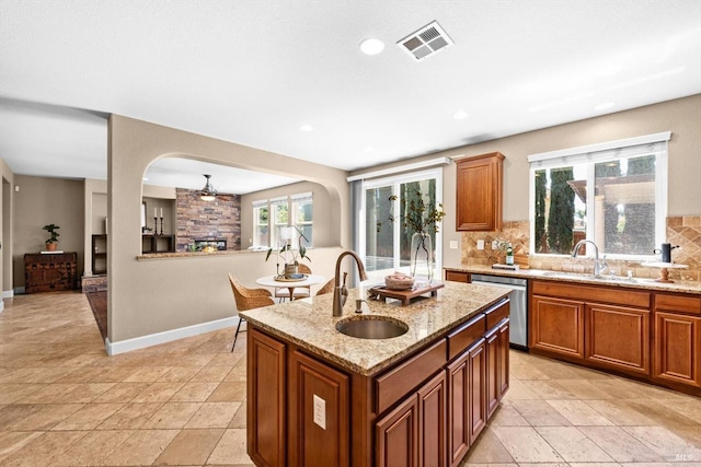 kitchen with stainless steel dishwasher, visible vents, brown cabinets, a sink, and backsplash