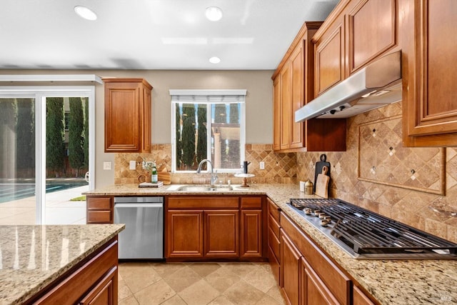 kitchen featuring brown cabinetry, decorative backsplash, under cabinet range hood, a sink, and stainless steel appliances