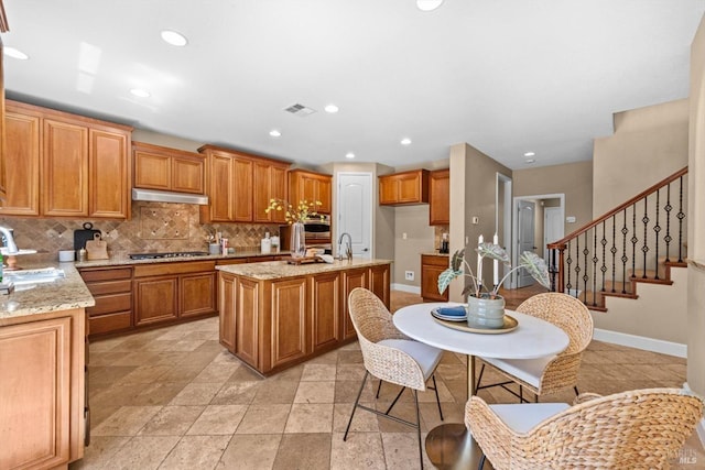 kitchen featuring visible vents, an island with sink, under cabinet range hood, backsplash, and stainless steel appliances