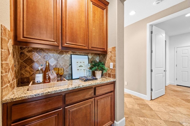kitchen featuring baseboards, backsplash, brown cabinets, and light stone counters